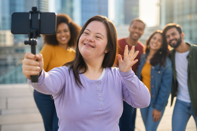 Mujer adulta con síndrome de Down grabando contenido con su smartphone en una ciudad moderna rodeada de personas sonrientes en un ambiente inclusivo
